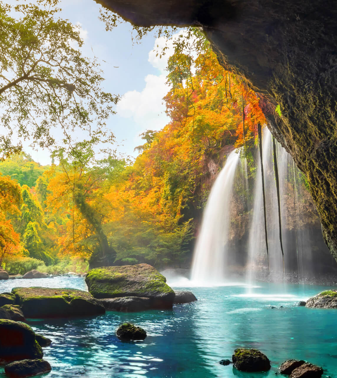 A waterfall behind crystal clear waters and rocks in a open jungle