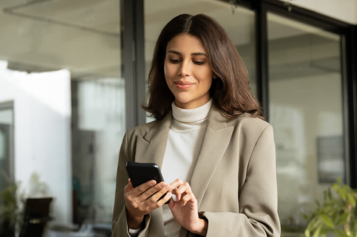 Lady smiling while holding and using a mobile phone in an office